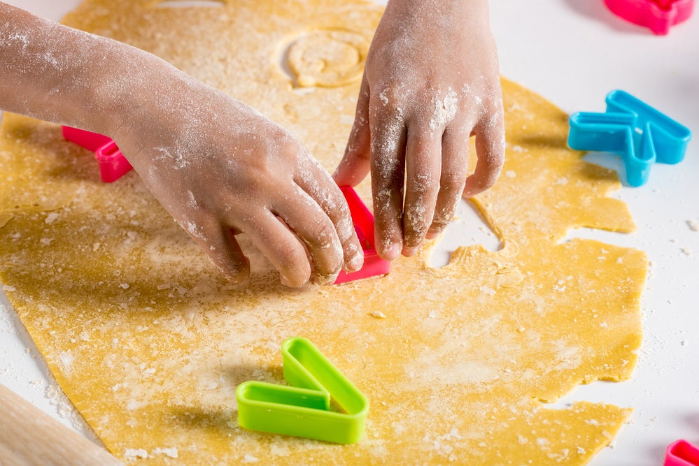 Child's hands using alphabet-shaped cookie cutters to create letters in dough