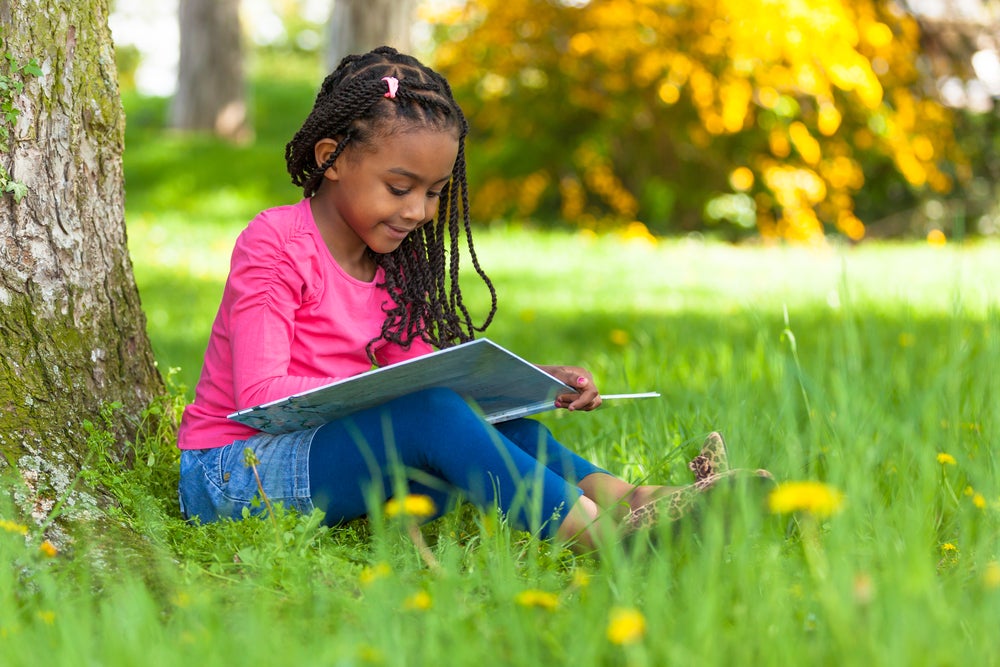 Girl reading a book outdoors in the grass under a tree
