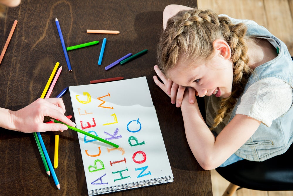 Child working on letter recognition as adult points to letters written in colorful pencil