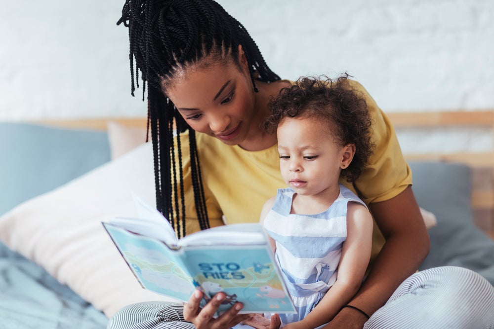 Mom sitting on bed helping her daughter with emergent literacy by reading to her