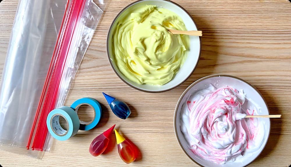 Materials for a sensory mixing bag activity; tape, food coloring, plastic bags, and bowls of colored shaving cream