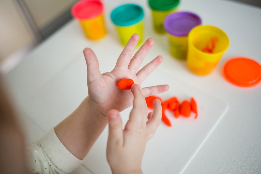 Child rolling play dough into a ball in her hand