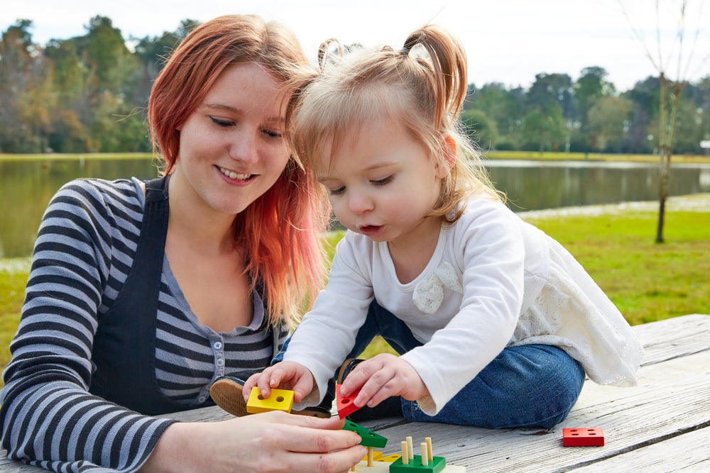 Mother and daughter playing with shape toys on a picnic table outside