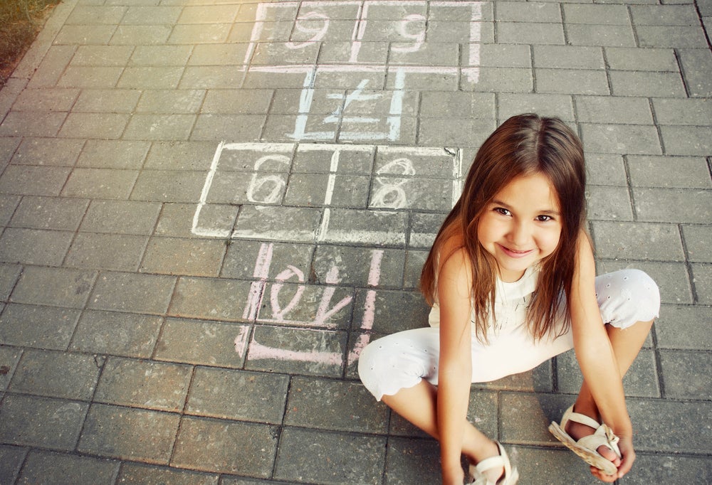 Smiling girl sitting on ground next to hopscotch grid