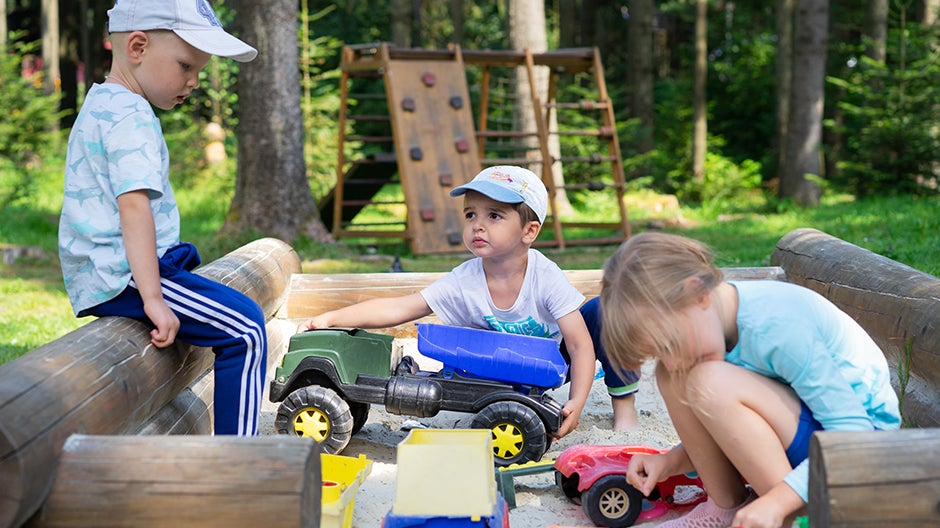 Three kids playing together with construction vehicle toys in a sandbox at a playground