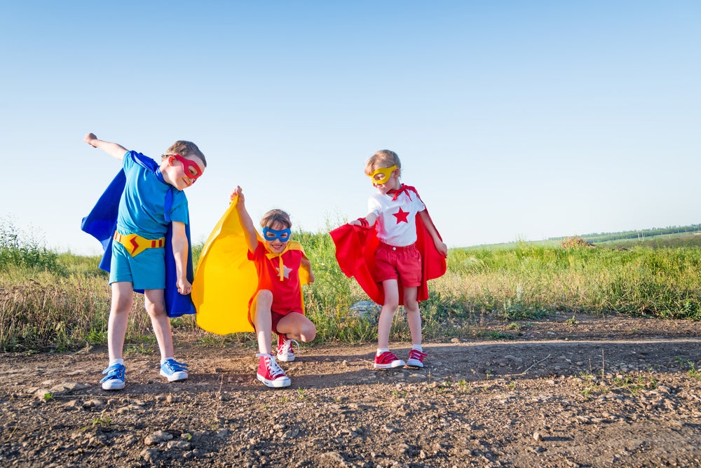 Three kids playing superheroes together in costumes