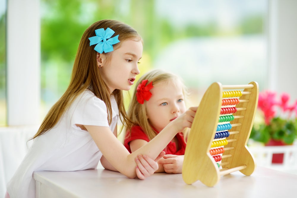 Two cute little girls playing with abacus at home. Big sister teaching her sibling to count. Smart child learning to count. Preschooler having fun with educational toy at home or kindergarten.