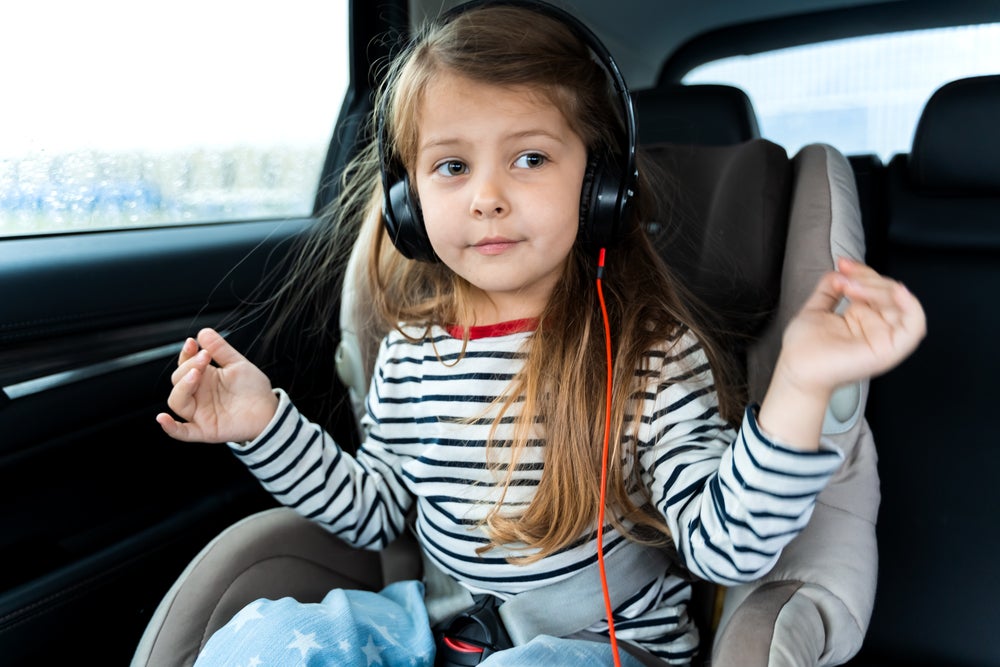 Young girl listening to music and dancing in car seat