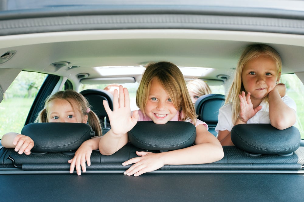 Three kids waving from the back seat of a car