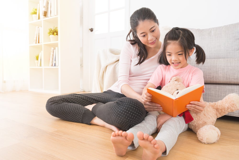 Mother seated on floor watching her daughter read a book at the right reading level