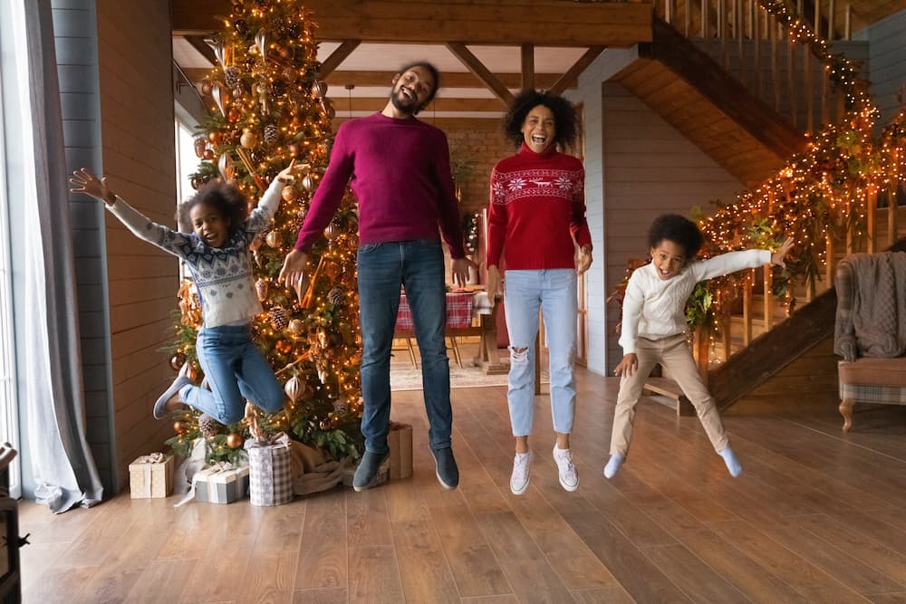 Family in sweaters jumping for joy with holiday decorations in background