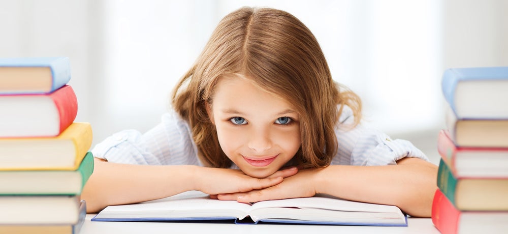 Girl smiling while resting her head on a book with other books around her
