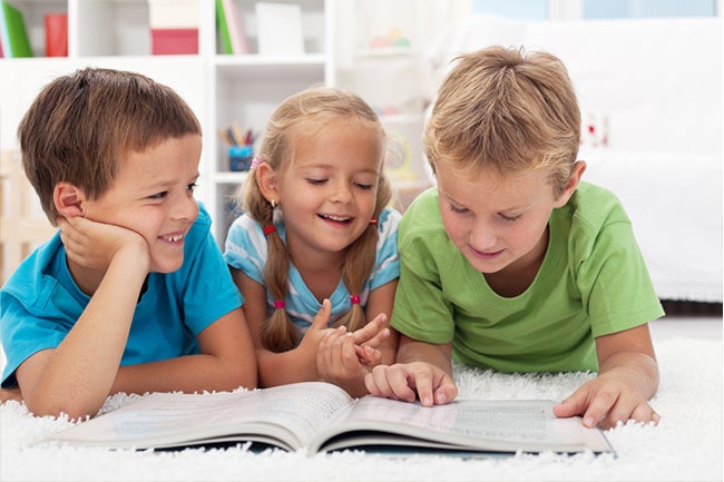 Three kids reading a book together on the floor in a playroom