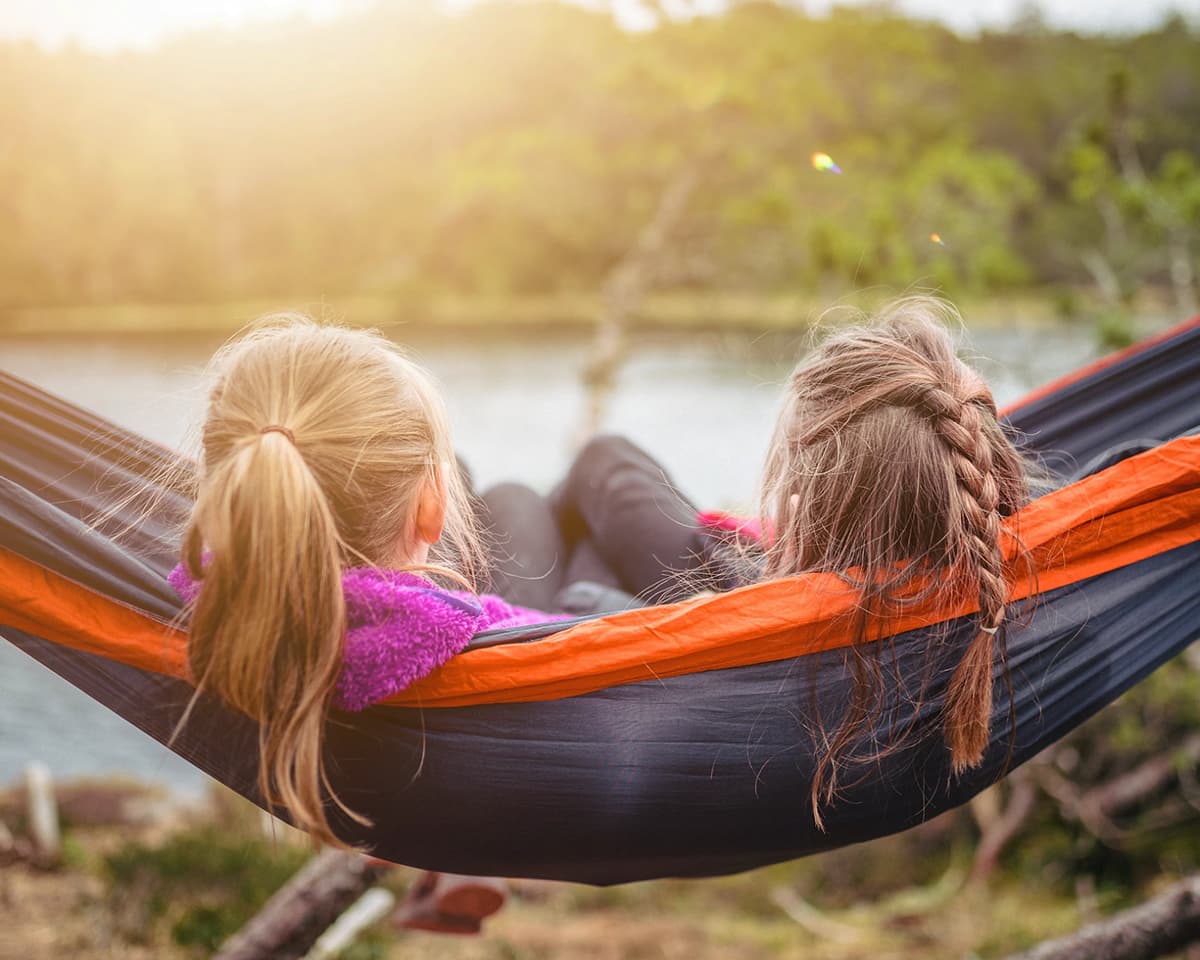 Two kid friends in a hammock overlooking a river at sunset