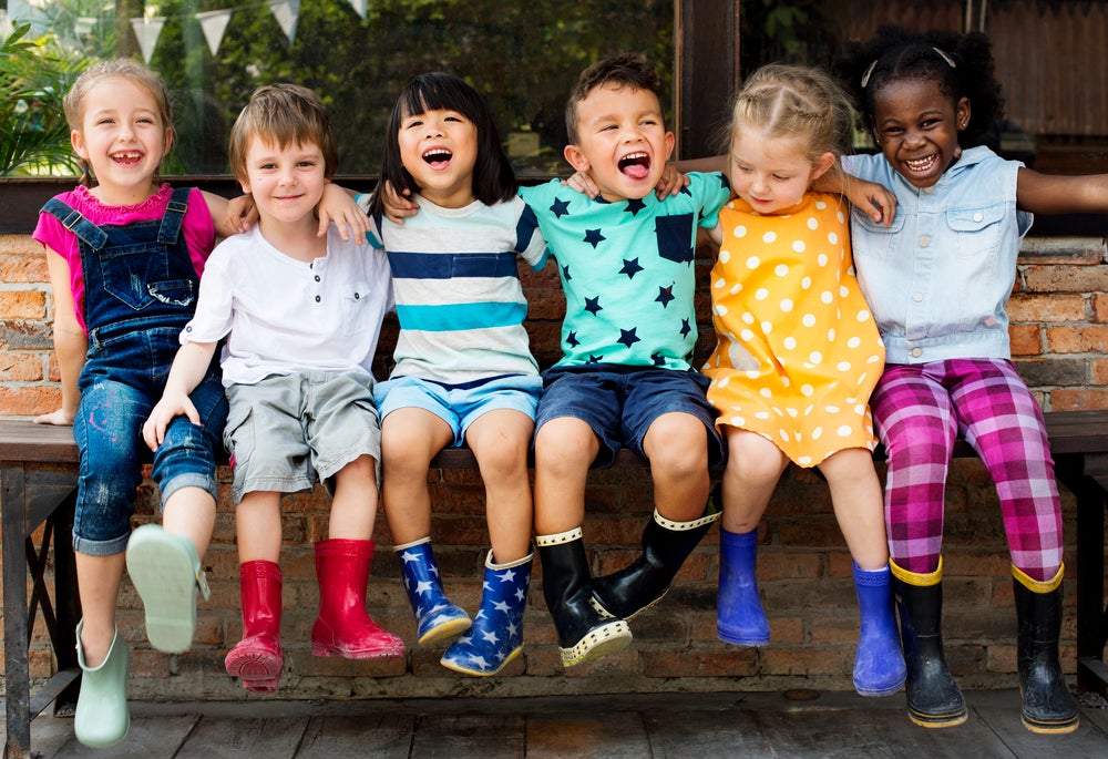 Group of kindergarten kids sitting on a bench, arms around each other, smiling