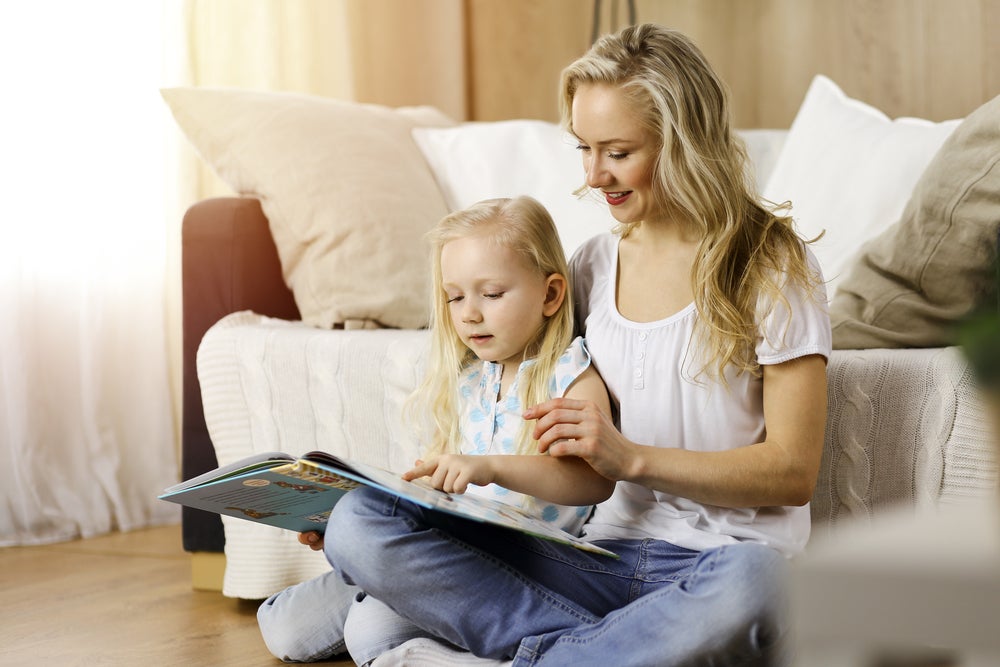 Mother reading book to daughter on the floor