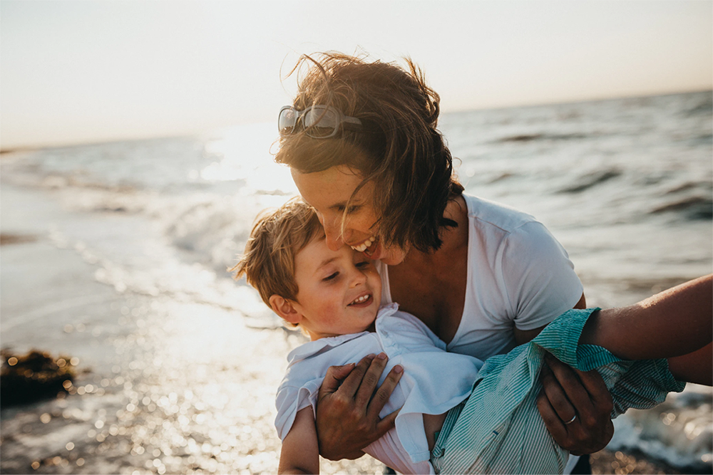 Mother holding child in arms while playing on the beach