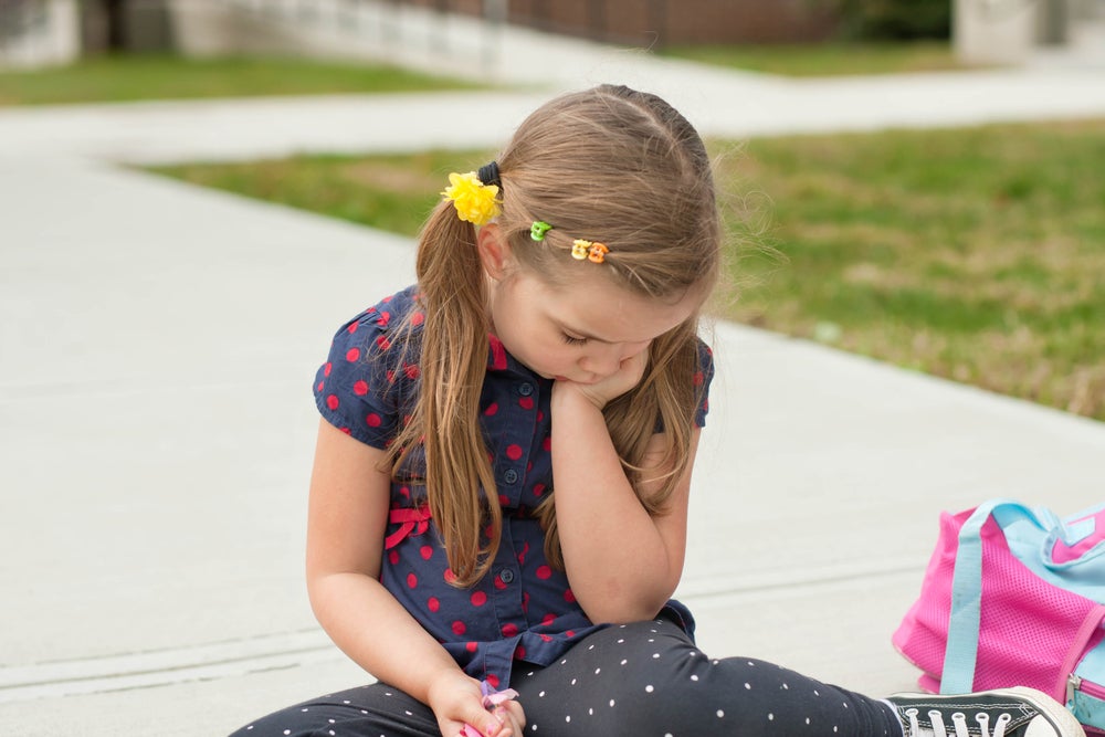 Shy girl sitting on sidewalk with head in hands