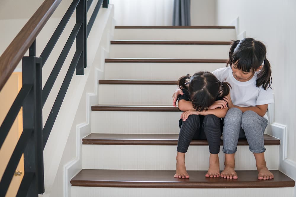 Girl comforting upset sister on staircase