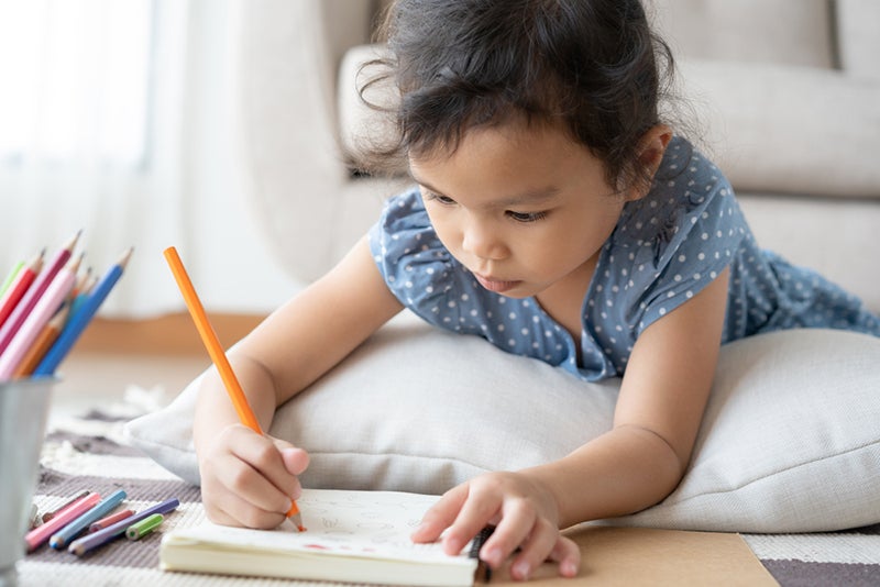 Child drawing in a sketchbook with a colored pencil
