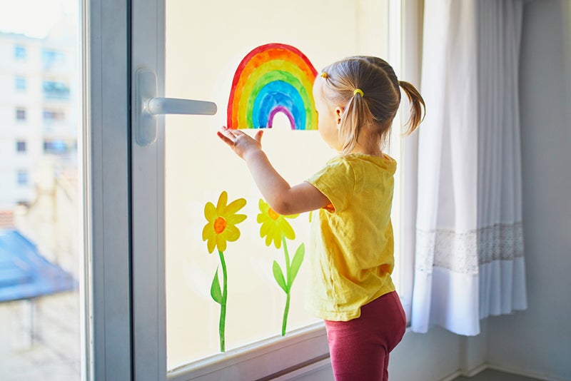 Child putting rainbow artwork on a large window
