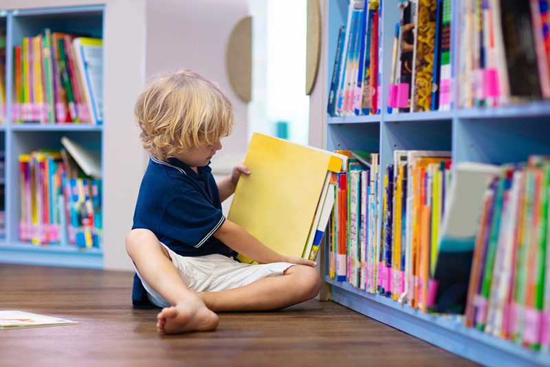 Child pulling book off shelf at library