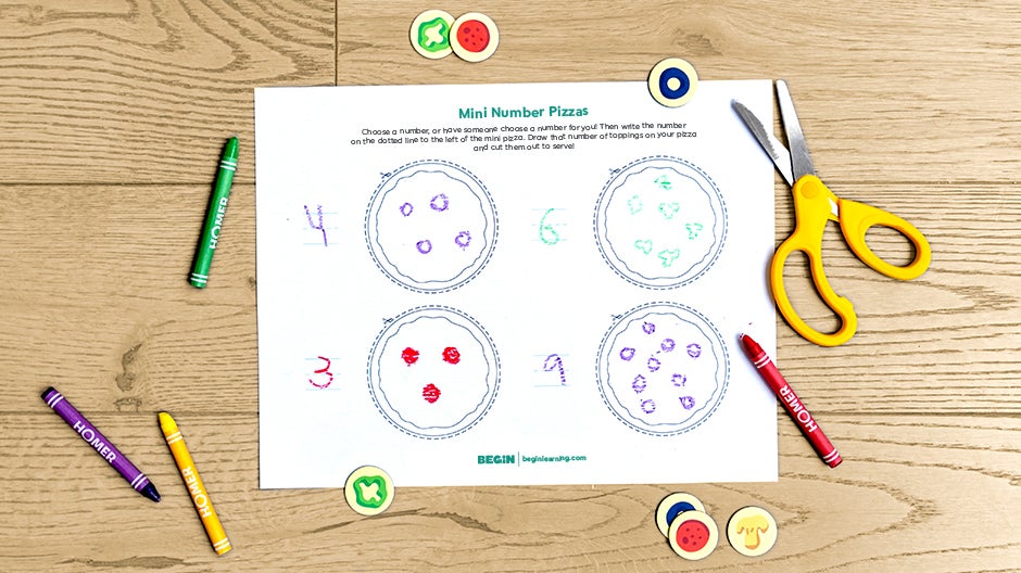 Completed Mini Number Pizzas printable on table with crayons, scissors, and pizza topping tokens