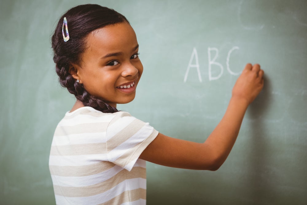 Smiling girl writing ABC's on blackboard