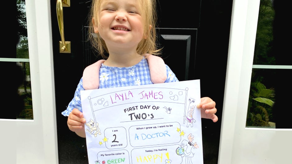Girl holding completed First Day of School printable, smiling while standing by front door