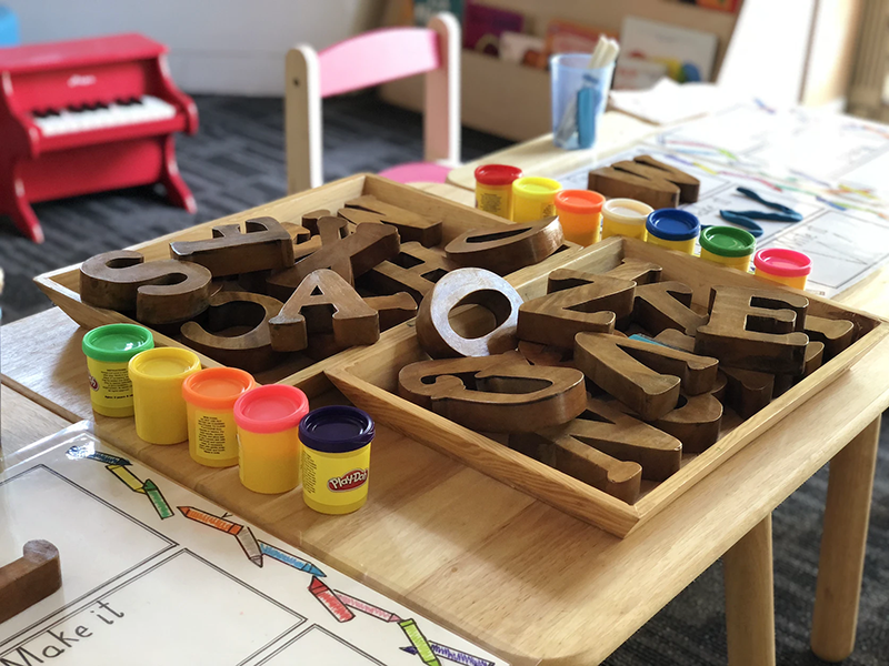 Table prepared for preschool activities with play dough and large wooden letters in trays