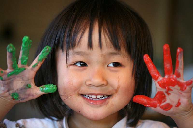 Child playing with bright red and green finger paints