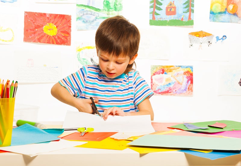 3-year-old boy cutting colorful paper with scissors in preschool art class