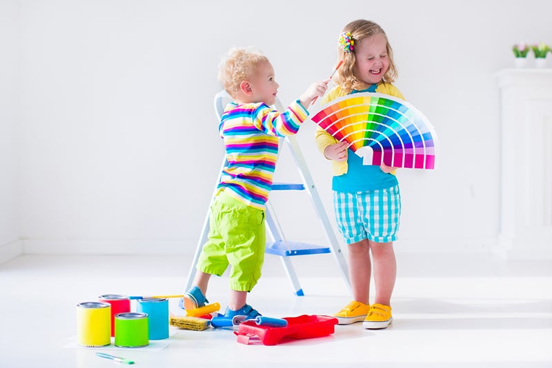Two kids playing with paint and a palette of bright color swatches in a white room