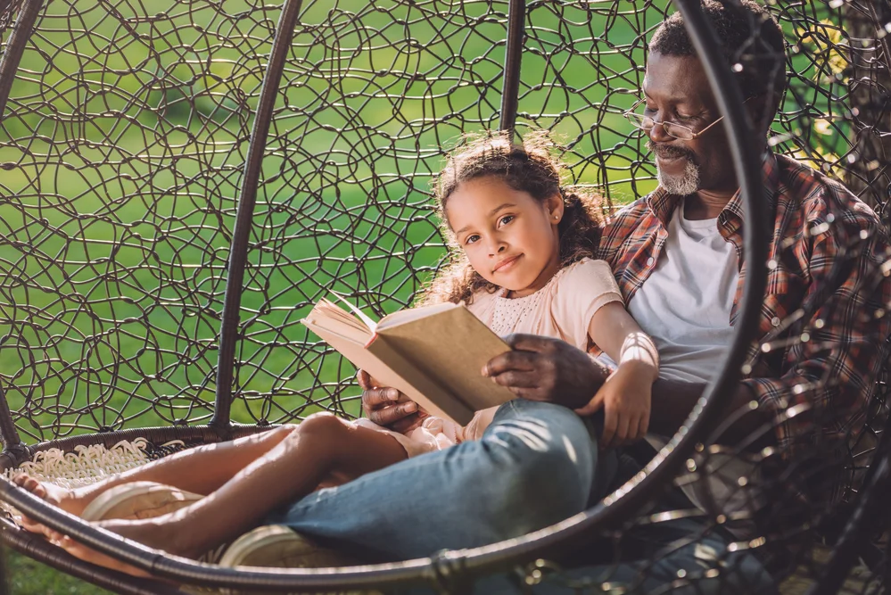 Adult reading to child outside in swing