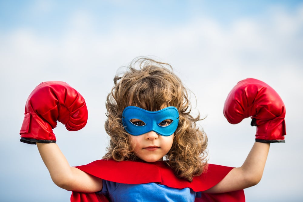 Girl dressed up like superhero in mask, cape, and boxing gloves