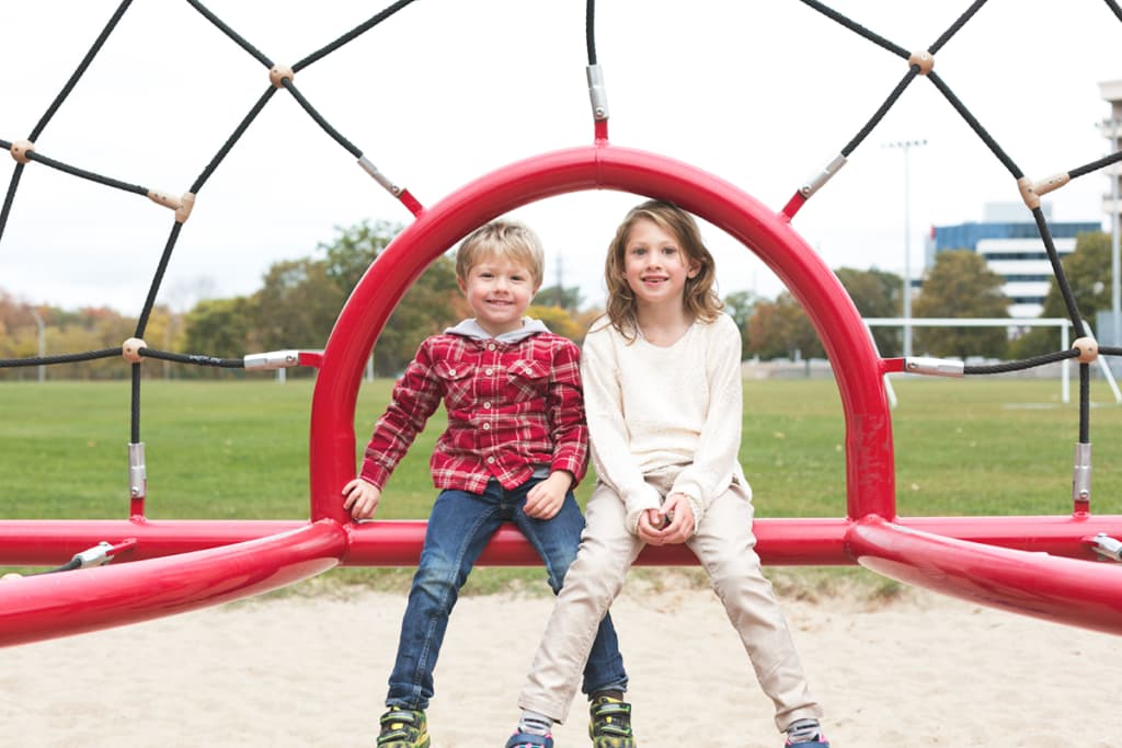 Two friends sitting together on a play structure outside