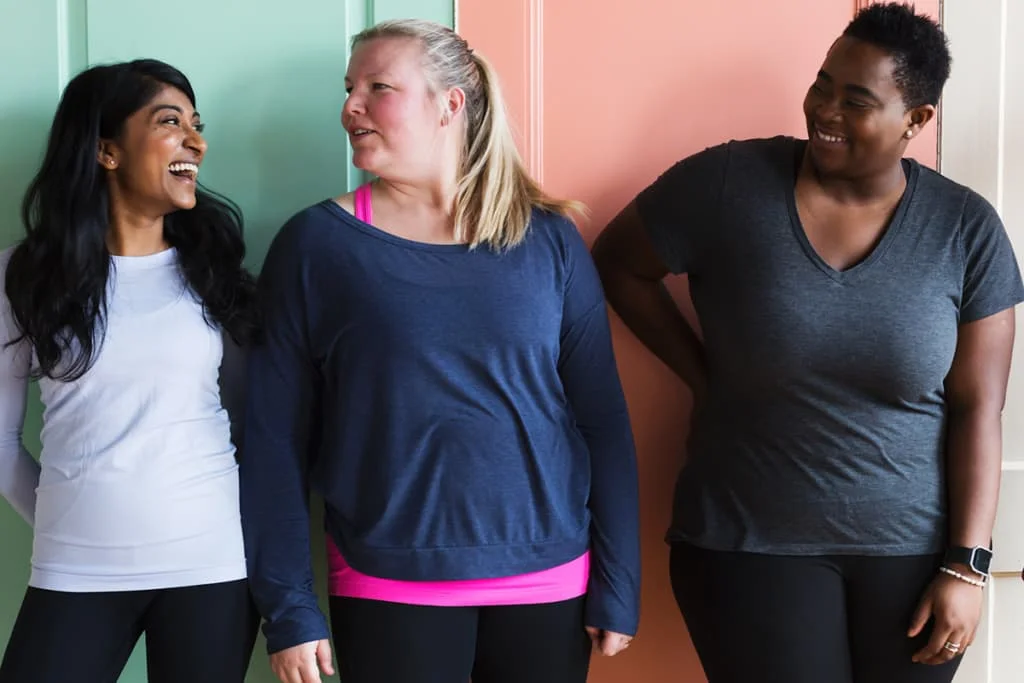 Three adult friends laughing together in a hallway