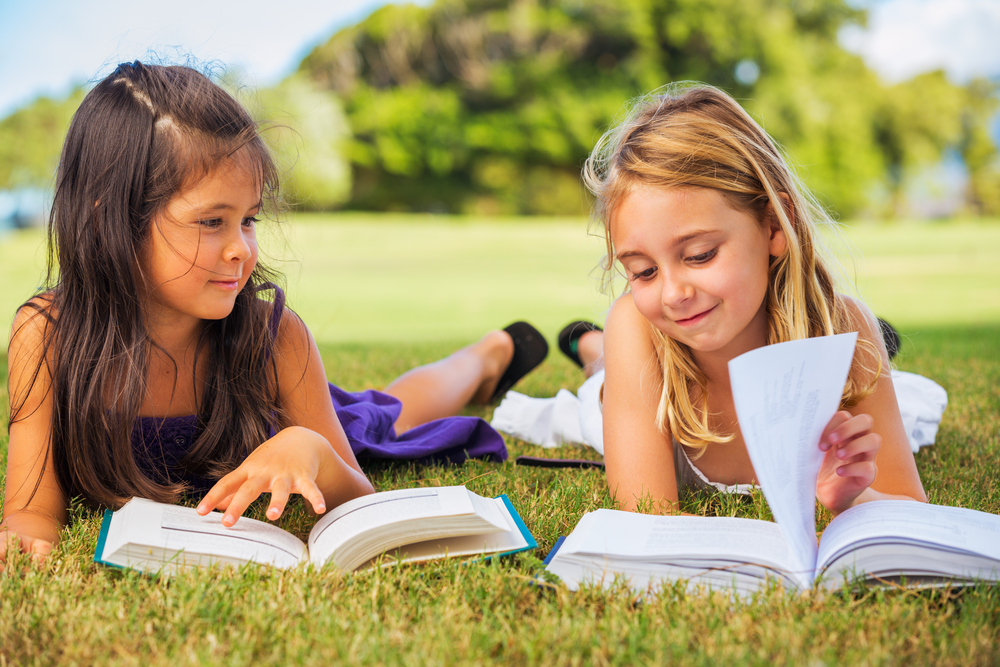 Two girls reading books outside on the grass