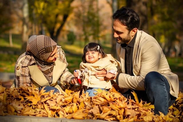 parents playing with child outside in the leaves