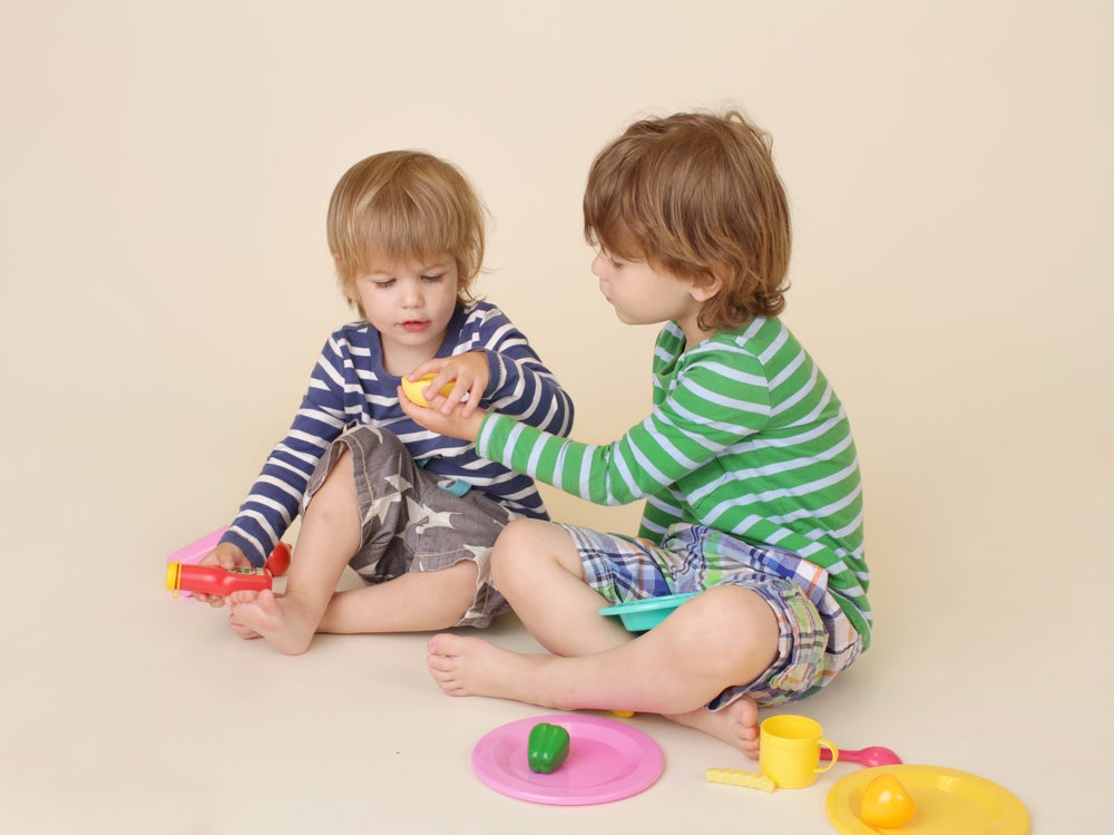 Two kids sharing pretend food while playing together on the floor