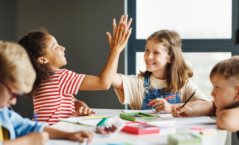 Kids high-fiving at a table in school