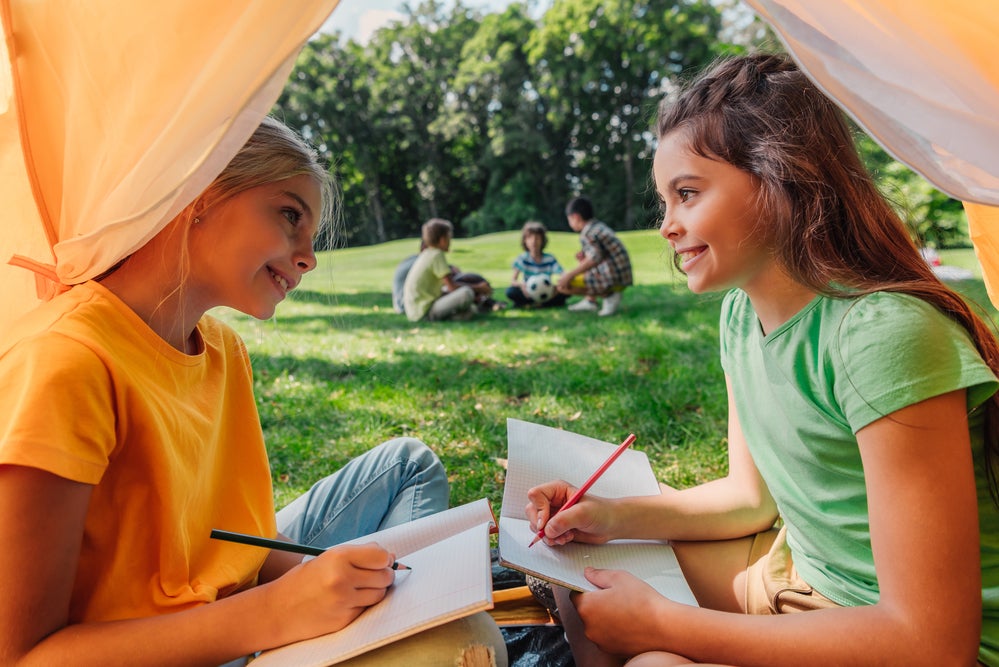 Two young girls writing a story together outside in a tent 