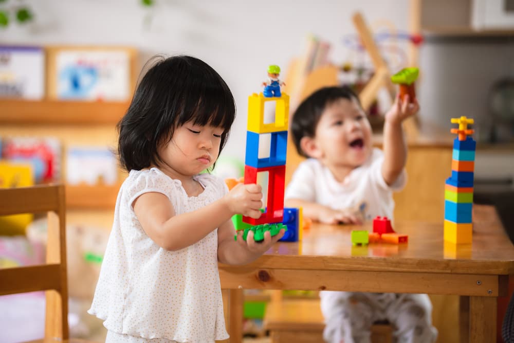 Two toddlers engaging in parallel play with toy bricks