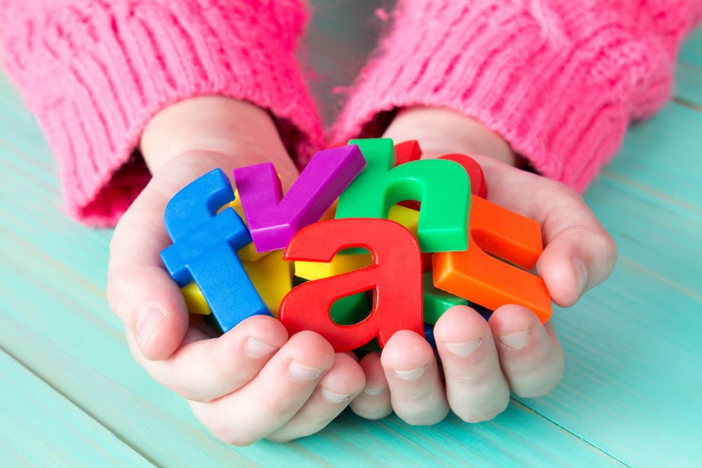 Child's hands holding a pile of colorful magnetic letters for learning phonograms