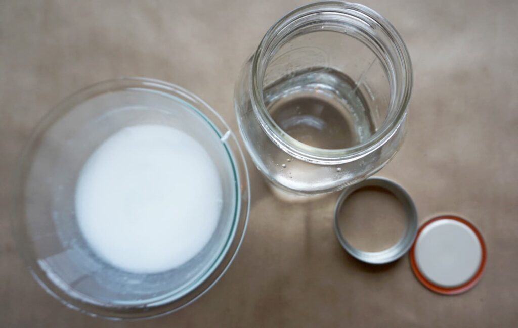 Mason jar filled with baby oil and cup filled with mixture of white paint and water