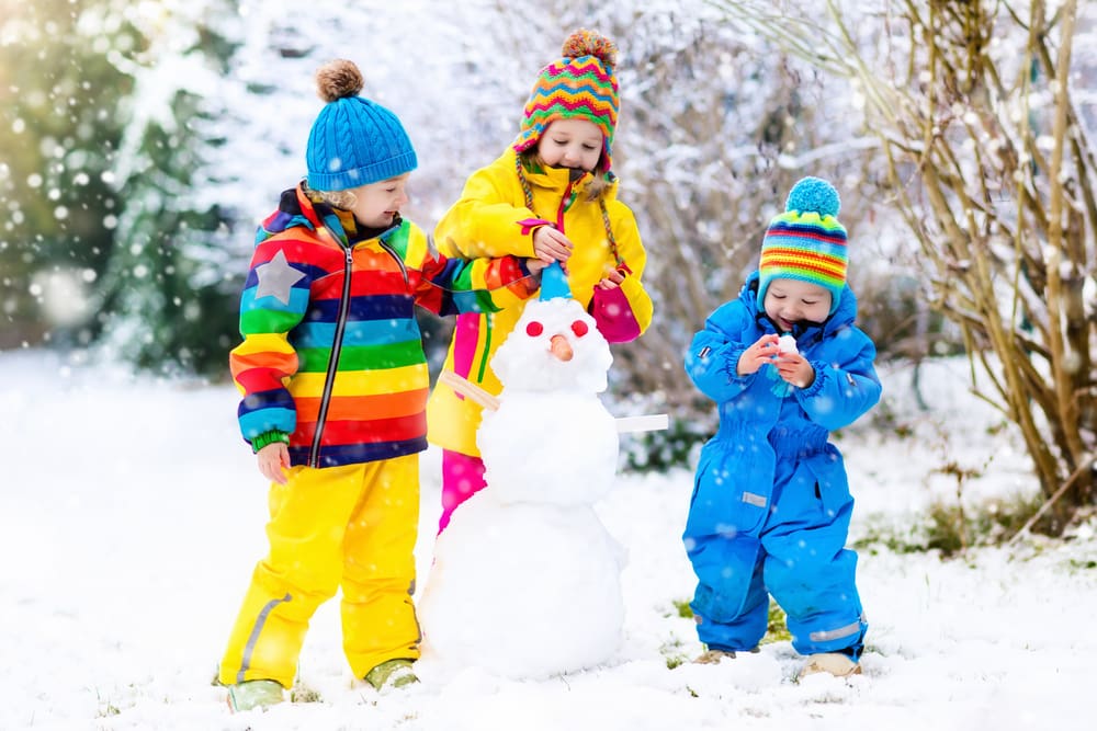 Three kids in brightly colored snowsuits building a snowman