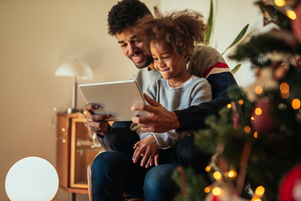 Father and daughter playing together on a tablet with Christmas tree in the foreground