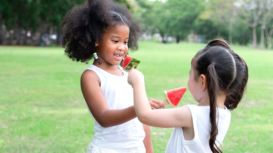 child happily sharing fruit with another child