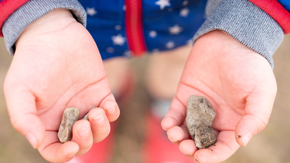 Child holding two rocks they found outside, an important part of a good early childhood education.