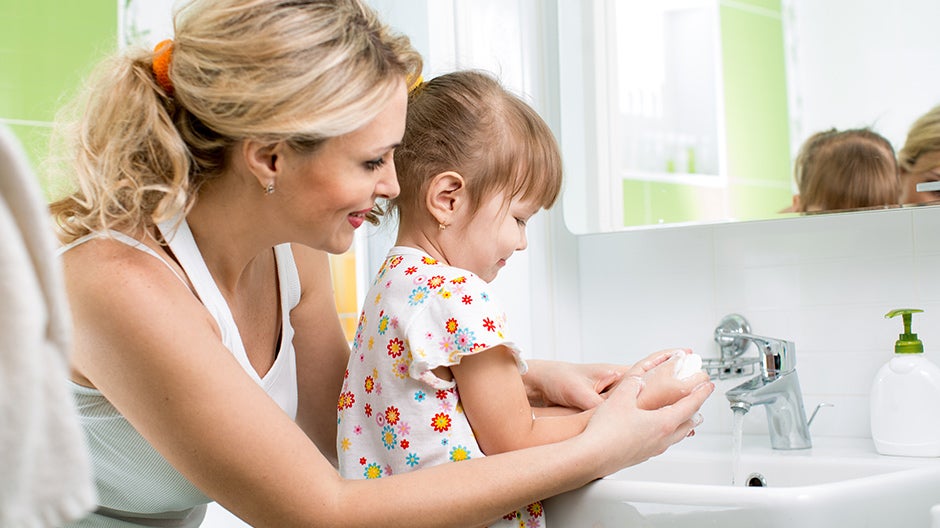 Child learning good habits by washing hands with her mother at home